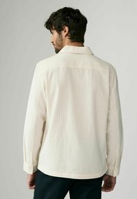 Light cream textured shirt with a grid pattern, long sleeves, and a classic collar. Features buttoned cuffs and a straight hem.