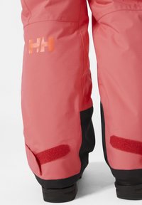 Pantalones de esquí rosa brillante con acentos negros, que cuentan con un logo reflectante, parches de Velcro y un acabado liso y texturizado.