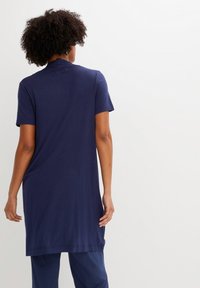 Vestido azul marino de manga corta con corte recto, textura suave y parte trasera ligeramente alargada. Presenta un cuello sutil y costuras mínimas.