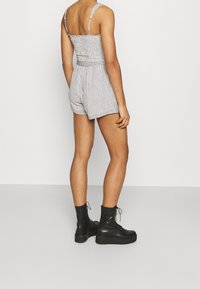 Zwart-wit geruit romper met dunne bandjes en een aansluitend lijfje, voorzien van een getailleerde taille en korte pijpen. Zwarte platform enkellaarsjes.