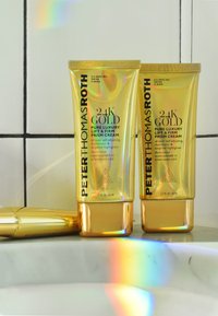 Guldrör med Peter Thomas Roth 24K Gold Prism Cream, med en blank yta, textdetaljer och en holografisk reflektion på en marmoryta.