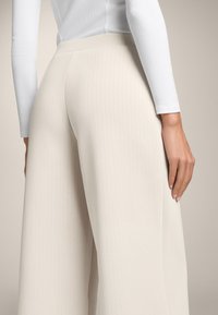 Pantalone širokog kroja u krem boji imaju rebrastu teksturu i dizajn s visokim strukom, u kombinaciji s prilagođenim bijelim vrhom s dugim rukavima.