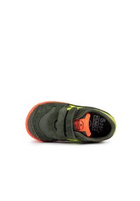 Zapatillas de tela verde con dos tiras de velcro, detalles en amarillo neón y suela de goma naranja. Superficie texturizada y plantilla acolchada visibles.