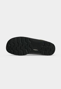 Semelle extérieure en caoutchouc noir d’une chaussure Keen avec des crampons profonds et le logo Keen au centre, présentée sur un fond clair uni.