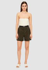 Top crema senza spalline abbinato a pantaloni corti plissettati verde scuro e una cintura nera. La modella indossa sandali bianchi slip-on. Design semplice e aderente.