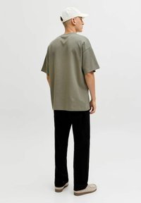 Prevelika olivno zelena majica s kratkimi rokavi, kombinirana s črnimi hlačami in bež čevlji. Na glavi je bela kapa.