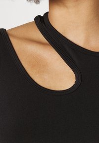 Top senza maniche nero con scollatura rotonda e dettaglio a fessura vicino alla spalla. Realizzato in tessuto morbido e elasticizzato con un design aderente.