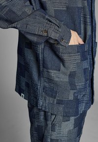 Marinblå skjorta med geometriska mönster, utrustad med knappmanschetter och en bröstficka; tillverkad av textil med varierande bredder och färger.