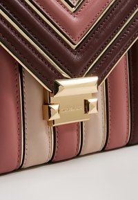 Bolso de cuero con un diseño en chevron en burdeos, rosa y beige. Herrajes metálicos dorados con un cierre cuadrado. Textura suave, acentos cosidos.