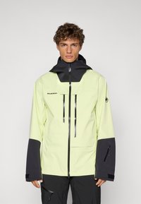 Veste imperméable jaune vif avec un col haut, des accents noirs, deux poches zippées à l'avant et des poignets élastiques. Logo de la marque visible sur la poitrine.