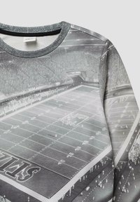 Grijze sweatshirt met een fotografische afdruk van een stadion, met details van het veld en het publiek vastgelegd vanuit een luchtperspectief.