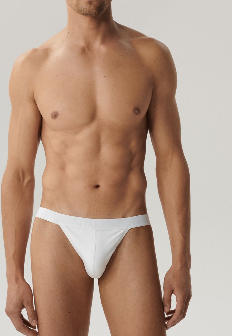 Białe stringi z miękkim elastycznym paskiem w talii, z delikatnym logo. Gładka faktura materiału, dopasowany krój. Bez wzorów ani akcentów.