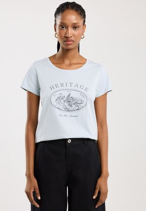 Světle modré bavlněné tričko s krátkým rukávem, kulatým výstřihem a černou květinovou grafikou s textem "HERITAGE". V kombinaci s černými kalhotami.