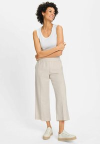 Light grey, wide-leg trousers with an elastic waistband, paired with a fitted white tank top and white sneakers, featuring a textured surface.