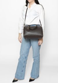 Borsa a tracolla in pelle marrone con una forma strutturata, doppi manici superiori e una tracolla rimovibile. Superficie testurizzata con accessori in tonalità oro.