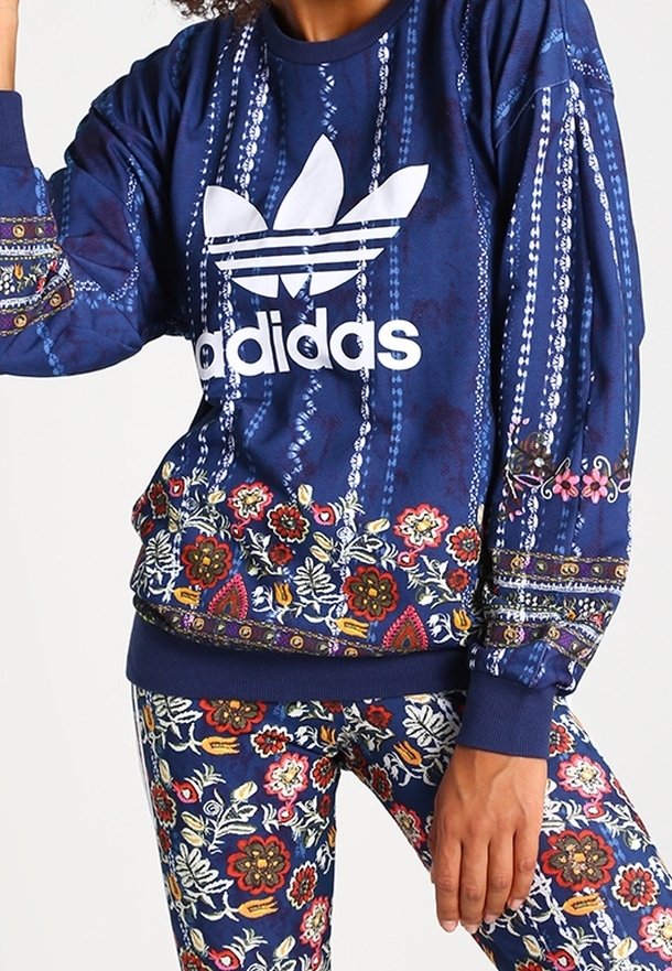Sudadera azul marino con un logo blanco de Adidas, patrones florales intrincados en el dobladillo y las mangas, junto con leggings a juego con el mismo patrón.
