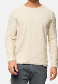 Pull en maille beige clair avec un col rond et des manches longues. La texture est lisse, avec un léger motif tissé.
