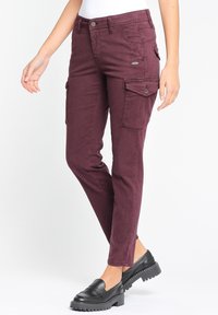 Burgundské cargo kalhoty s mnoha kapsami, slim-fit střihem a prošívanými detaily. Nosené s černými mokasíny s masivní podrážkou.