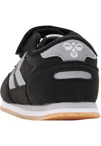 Scarpa sportiva nera realizzata in pelle scamosciata e mesh, con un accento grigio del logo, chiusura con cinturino elastico e suola intermedia bianca con suola in gomma.