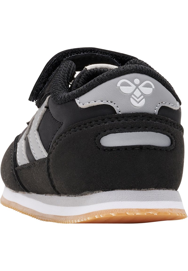 Chaussure de sport noire en matériaux suédé et mesh, dotée d'un accent de logo gris, de fermetures à bande élastique et d'une semelle intermédiaire blanche avec une semelle en caoutchouc couleur gomme.