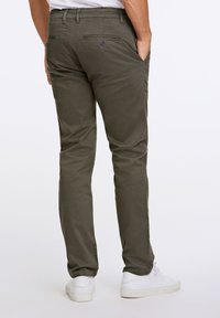 Olive green chinos o slim fit, wykonane z bawełny. Posiadają tylne kieszenie z zapięciem na guziki oraz gładką teksturę, w połączeniu z białymi butami.