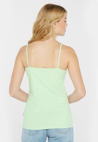Mintgrünes Trägershirt mit dünnen Trägern, aus weicher Baumwolle gefertigt. Besitzt ein tailliertes Design und einen geraden Rückenschnitt. Keine Muster oder Akzente.