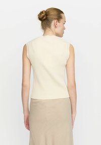 Ärmlös ribbad topp i en ljus krämfärg, med en figurnära design och rak fåll, i kombination med en beige kjol.