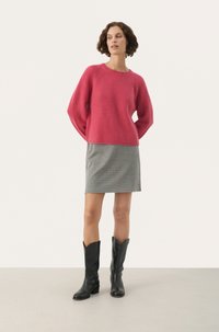 Różowy sweter ribbed z opadłymi ramionami, w połączeniu z czarno-białą spódnicą w kratę i czarnymi kowbojkami do kolan.