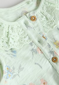 Light green top made of soft fabric, featuring floral patterns in blue and pink, lace trim around the neckline, and wooden button closure.