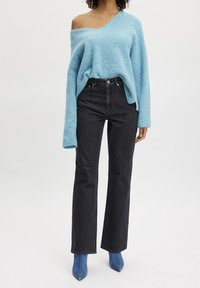 Pull tricoté oversize bleu clair avec une épaule dénudée, associé à un jean noir taille haute à jambes droites et des bottines bleues pointues.