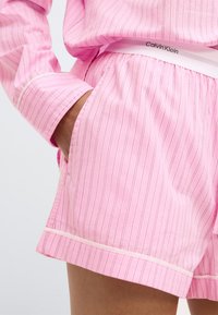 Ροζ βαμβακερά σορτσάκια με λεπτές κάθετες ρίγες, ελαστική μέση με λογότυπο "Calvin Klein" και αντίθεση στην περιφέρειά τους.