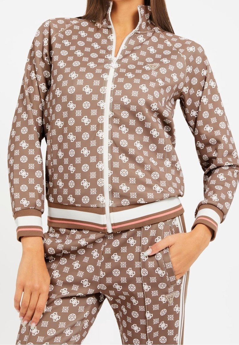 Chaqueta marrón con cremallera y diseño en patrón blanco, con un cuello alto, puños de rayas en blanco y rosa, y pantalones a juego. Textura de tela suave.