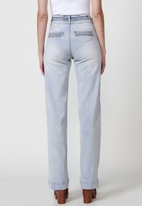 Jeans taille haute bleu clair avec un design de poche arrière tressée. Jambes droites et détail de ourlet retroussé. Texture en denim lisse.