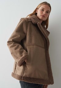 Bruine faux shearling jas met een brede kraag, zijzakken en een getextureerde binnenkant. Heeft een recht model en pluche afwerking langs de randen.