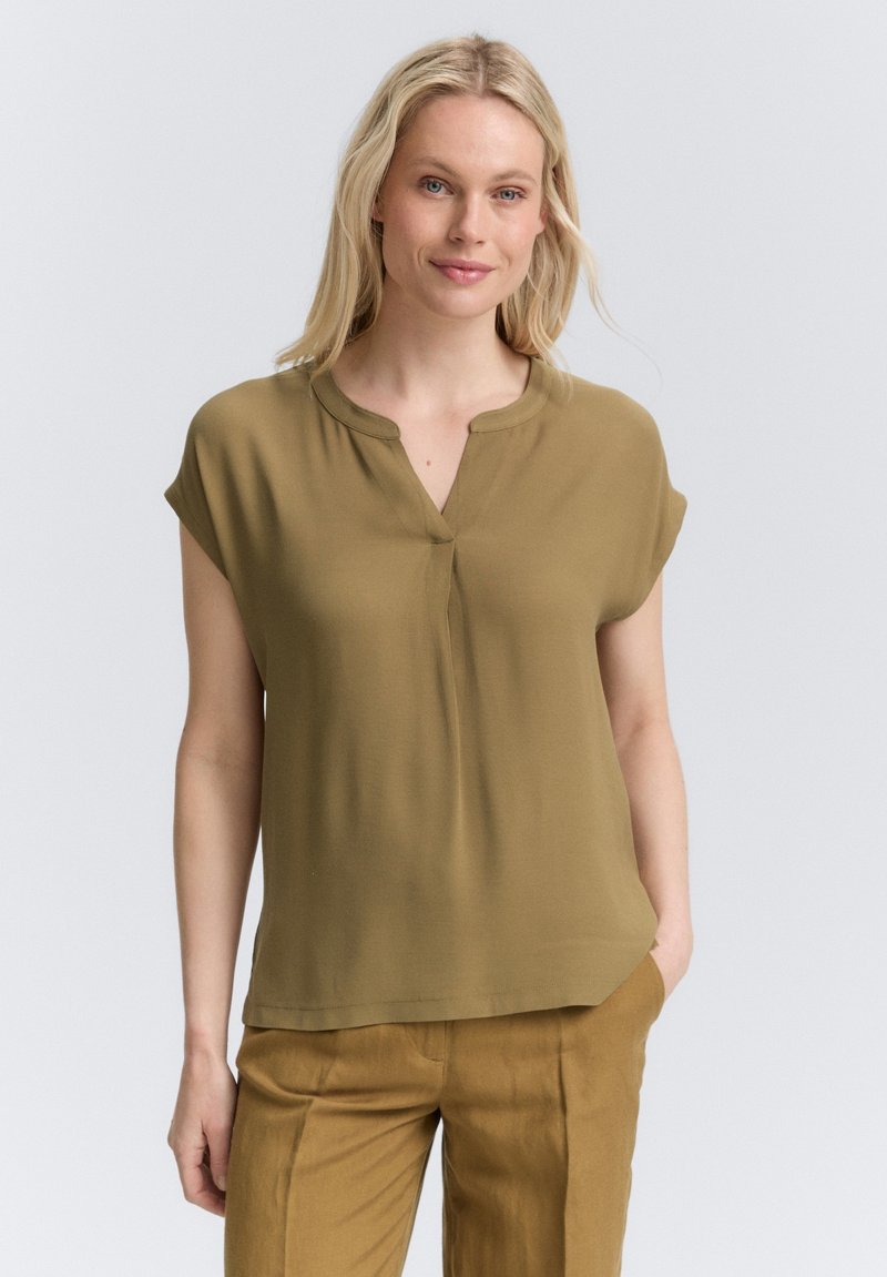 Blouse vert olive avec un col mandarin, des manches courtes et une coupe ample. Tissu lisse avec un léger éclat, sans motifs ni accents.