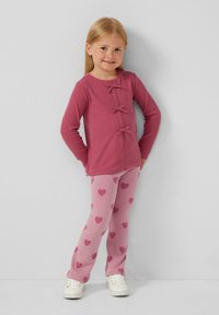 Rosa gerippte Langarmbluse mit drei Schleifenakzenten, kombiniert mit hellrosa Hosen mit Herzmustern. Beide aus einem weichen Stoff.