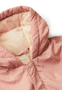 Světle růžová prošívaná bunda s bílými puntíky, vybavená pohodlnou kapucí a měkkou podšívkou. Viditelná nálepka: "United Colors of Benetton."