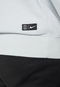 Sudadera azul clara con dobladillo y puños acanalados. Cuenta con un parche negro con el logo blanco de "París" y el Swoosh de Nike en la parte inferior del frente.