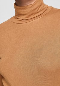 Tan-paita, jossa on ribbitekstuuri, slim fit ja korkea kaulus. Kangas näyttää sileältä ja joustavalta.