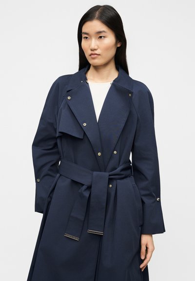 Μακρύ παλτό μπλε ναυτικό με ζώνη στη μέση, μεγάλο γιακά και κουμπιά με κουμπώματα. Λείο υλικό με πτυχώσεις στην περιοχή του στήθους.
