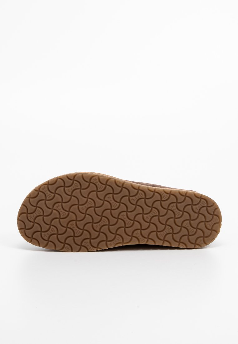 Hellbraune Gummisohle mit einem gewellten Profilmuster, versehen mit geprägtem Markentext. Glatte Oberfläche mit leichtem Glanz.