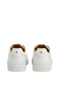 Zapatillas blancas con un acabado de cuero suave, collar acolchado y un interior marrón claro. Con un pequeño logo en la parte trasera.