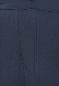 Tela azul marino con una textura suave, que presenta una cinturilla fruncida y bolsillos laterales. El diseño incluye pliegues sutiles a lo largo de los lados.