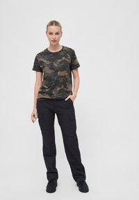 Sötétzöld, barna és szürke terepmintás pamut póló, fekete oldalzsebes cargo nadrággal és erős fekete lábbelivel párosítva.