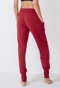 Rode joggingsbroeken van zacht materiaal, met een elastische tailleband, twee zijzakken en aansluitende boorden bij de enkels. Eenvoudig design, gladde textuur.