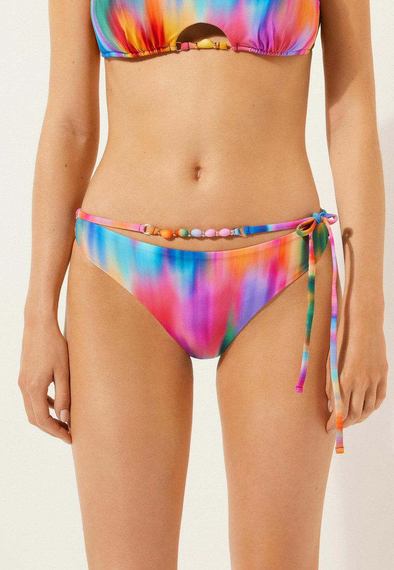 Färgglad bikiniunderdel med knyt i sidan, som har en flerfärgad gradient av rosa, blått, orange och lila. Pärlprydnad vid midjan.