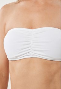 Balts bandeau tops, kas izgatavots no gludas auduma, ar savilkuma detaļām centrā. Vienkāršs, bezšuvju dizains bez siksniņām.