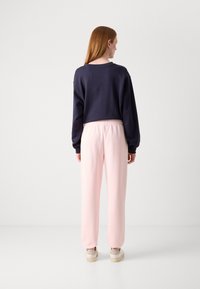 Mikina v námořnické modři, zkrácený design; spárována s růžovým teplákovým kalhotami s elastickým pasem; model má na sobě béžové boty.