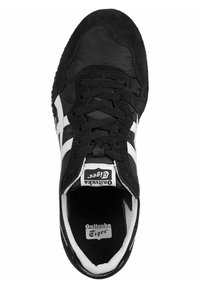 Black sneaker with textile and suede upper, featuring white stripes on the sides, lace-up closure, and a textured rubber sole.