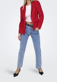 Rød tekstureret blazer over en hvid crop top, kombineret med lyseblå højtailede jeans og sorte spidse hæle. Med guldfarvet hardware.